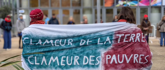 2. novembre 23 deux militant.e.s de Lutte et Contemplation de dos portent une banderole marquée "Clameur de la Terre et Clameur des Pauvres, Luc" en lettres blanches sur des calques bleus et rouges