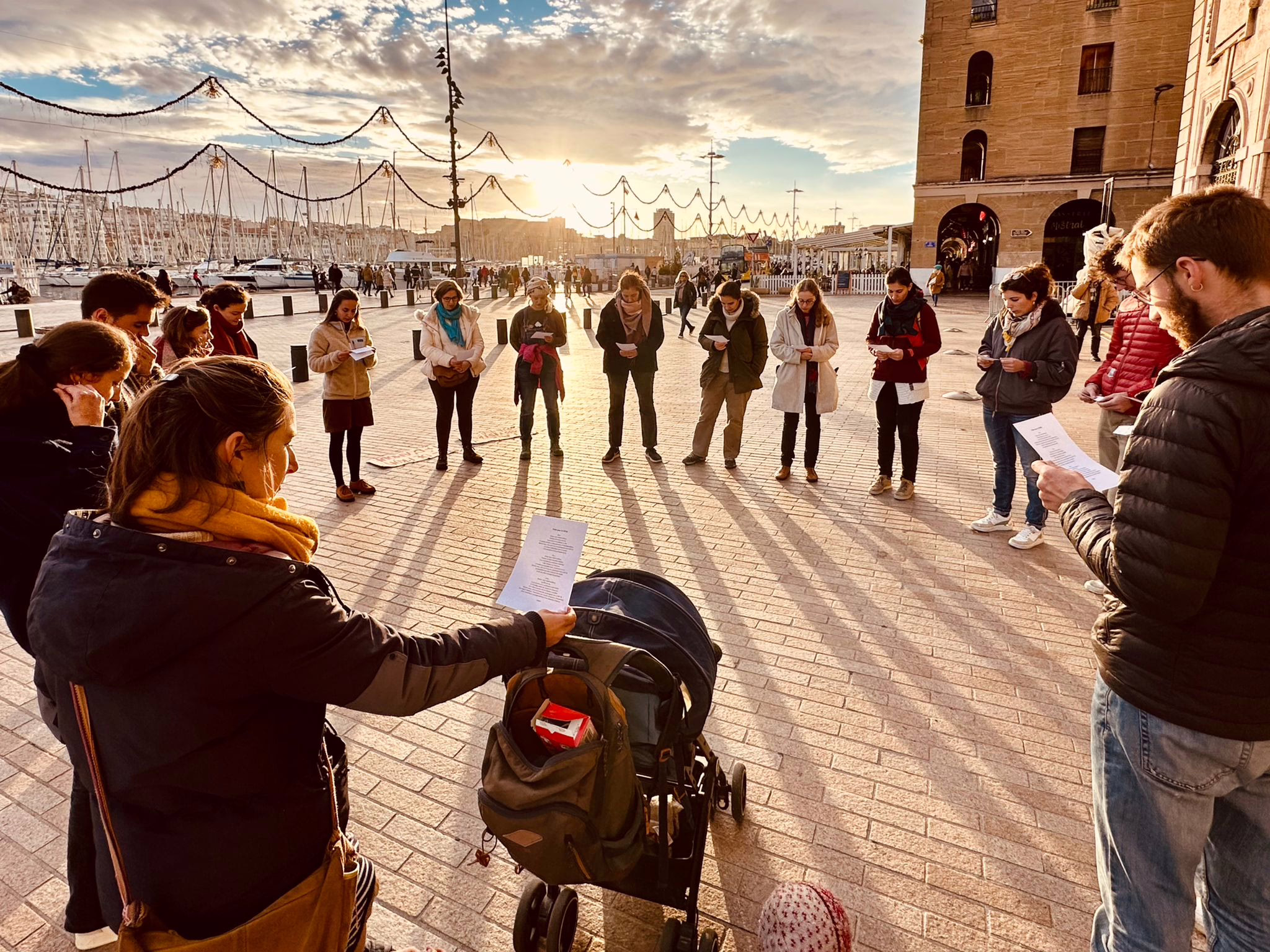 un groupe de militants de Lutte et contemplation en cercle de silence sur le port de la Rochelle, en contre-jour avec une lumière rasante et un soleil couchant sur le port en arrière plan