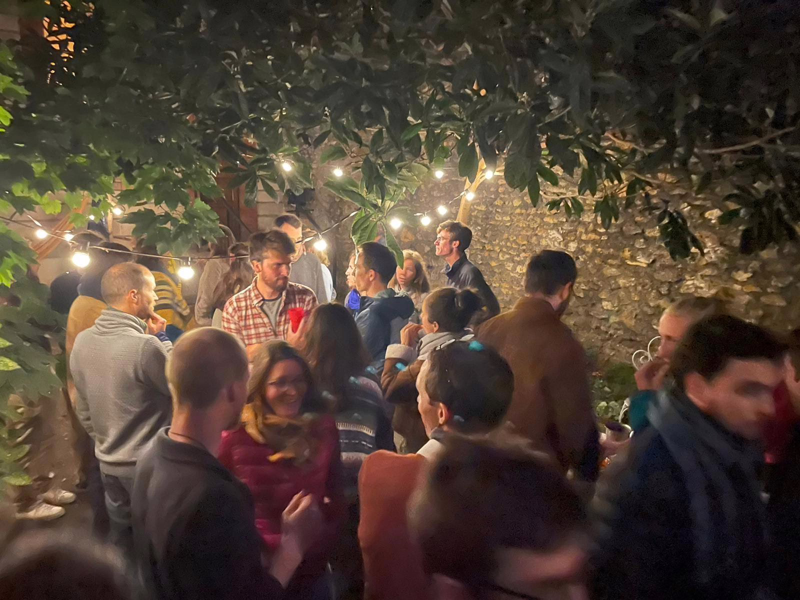 Soirée au Dorothy avec des membres et sympathisants de Lutte et Contemplation qui discutent sous un arbre plein de lanternes allumées. La scène a une ambiance chaleureuse